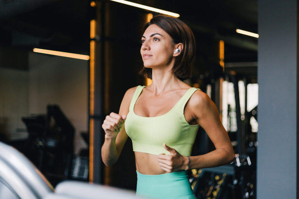 fit caucasian beautiful woman in fitting sport wear at gym running jogging at treadmill with wireless headphones in ears